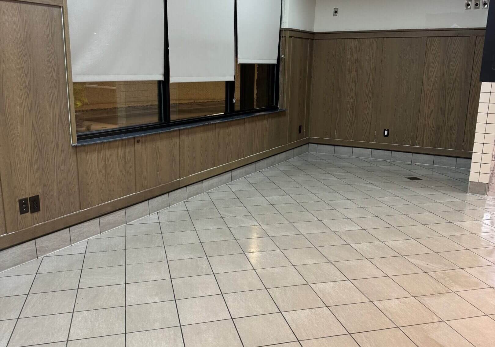 Empty tiled room with wood paneling and white blinds.