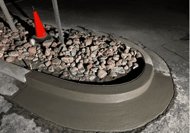 Freshly poured concrete curb surrounding a rock bed with an orange cone.